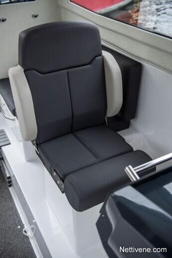 A black and gray marine boat seat with armrests, located indoors near a window overlooking water.